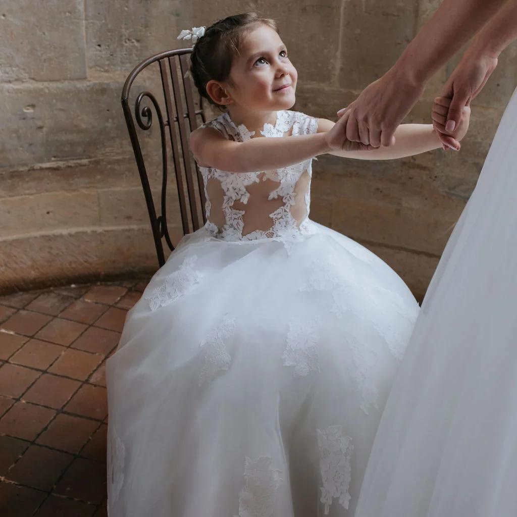 une petite fille en robe de mariée qui tient la main à sa maman