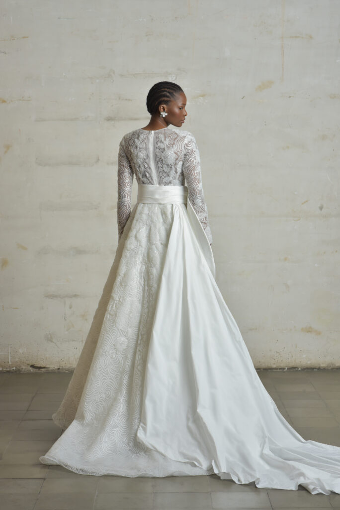 femme portant une robe de mariée princesse glamour et manches longues, avec un joli nœud au niveau de la taille