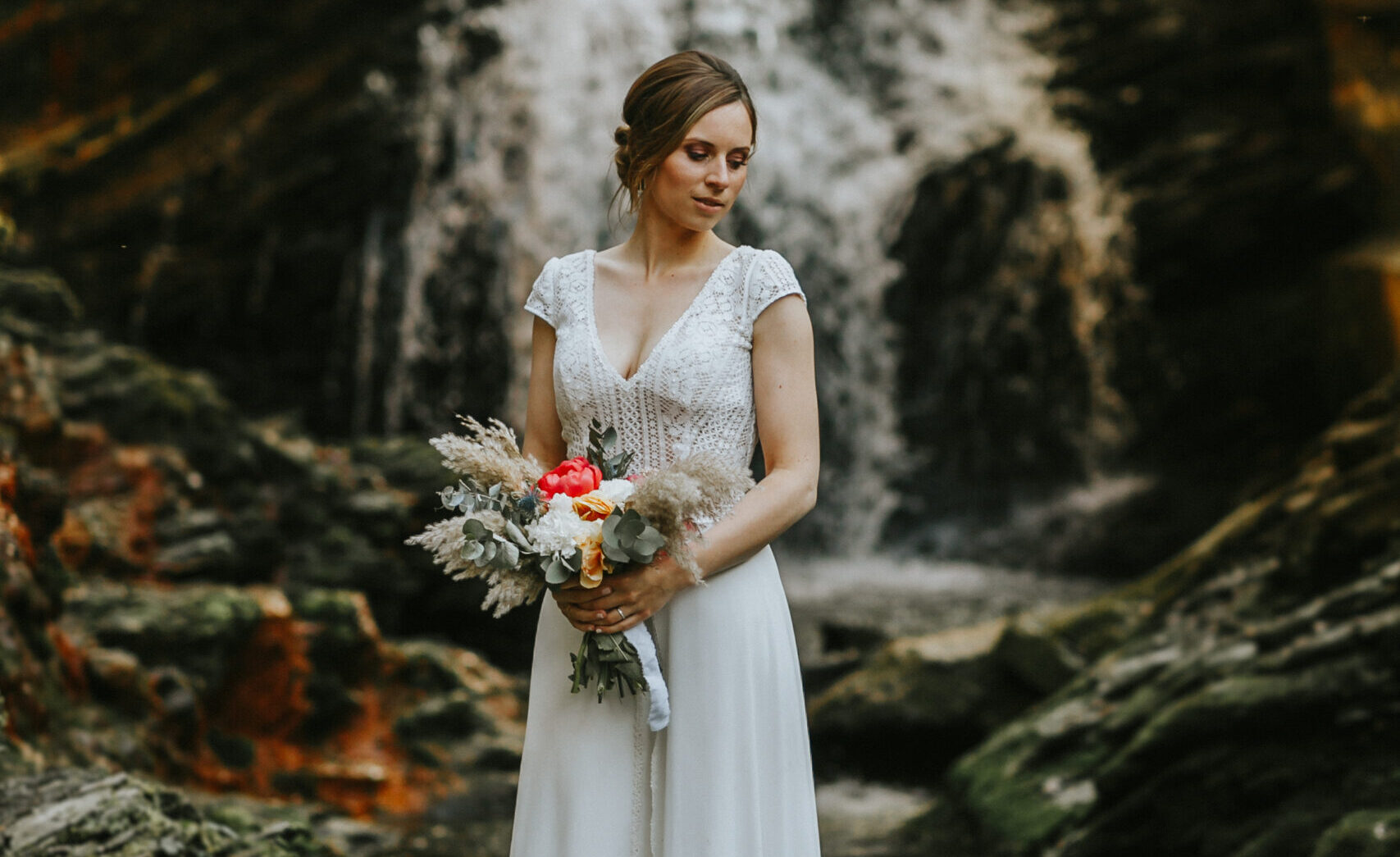 femme dans une robe de mariée dans un décor automnal devant une cascade dans la forêt