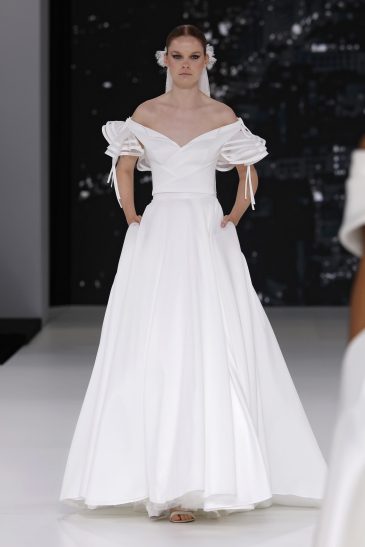 femme dans une robe de mariée à col sur un podium de défilé