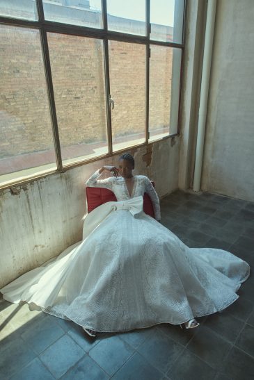 femme assise portant une robe de mariée princesse glamour et manches longues, avec un joli nœud au niveau de la taille