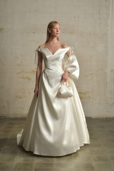 femme dans une robe de mariée princesse en mikado avec un grand nœud et un sac à main