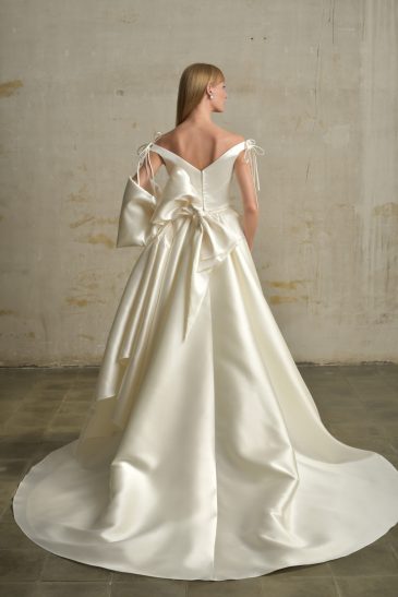 femme dans une robe de mariée princesse en mikado avec un grand nœud et un sac à main