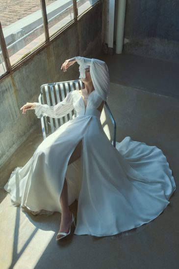 femme assise habillée d'une robe de mariée fluide raffinée à fente et à manches longue en mousseline plissé
